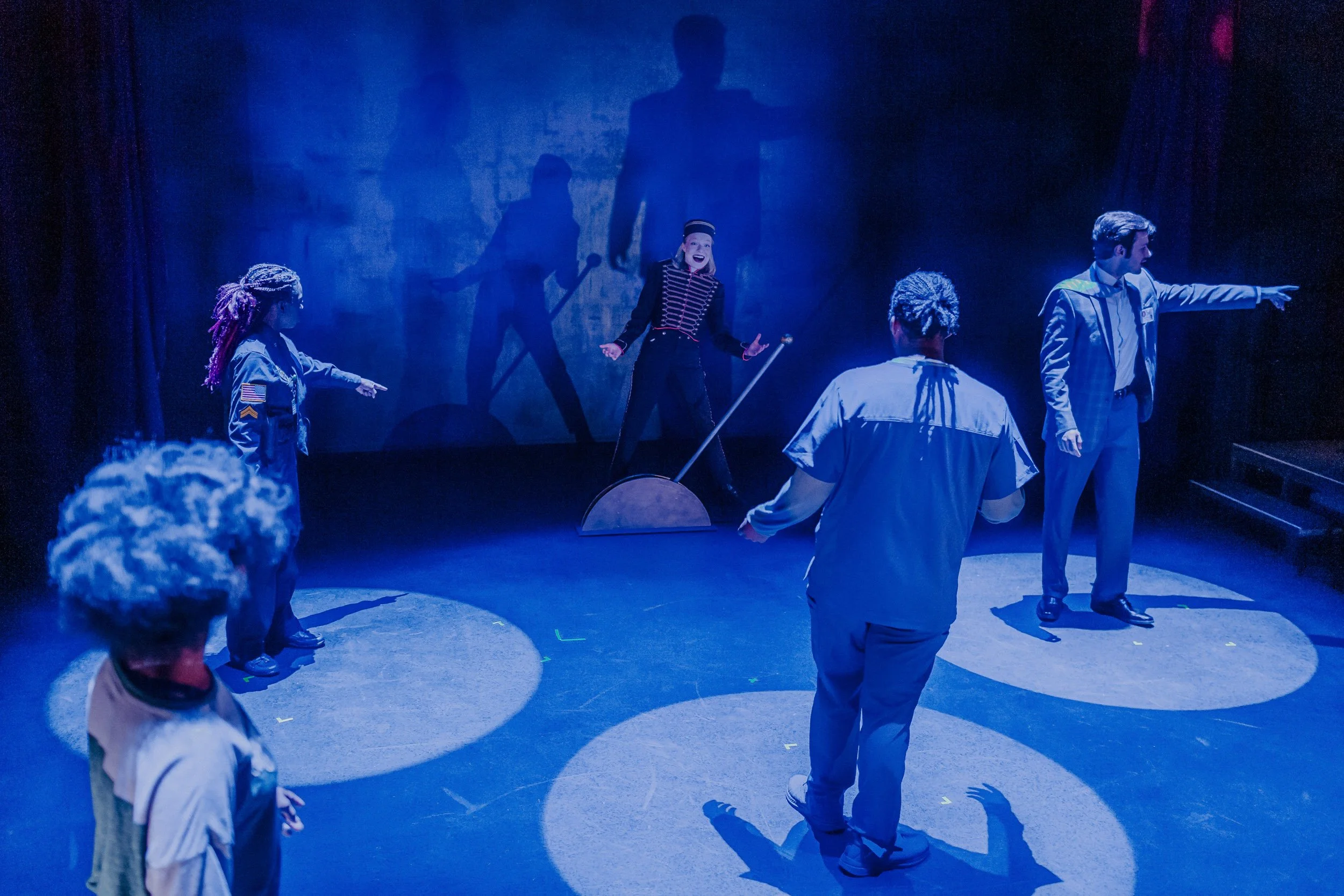 Theatrical performance with Olivia Scott, actress and performer, including a clown, under dramatic lighting with shadows on the backdrop in Everybody production