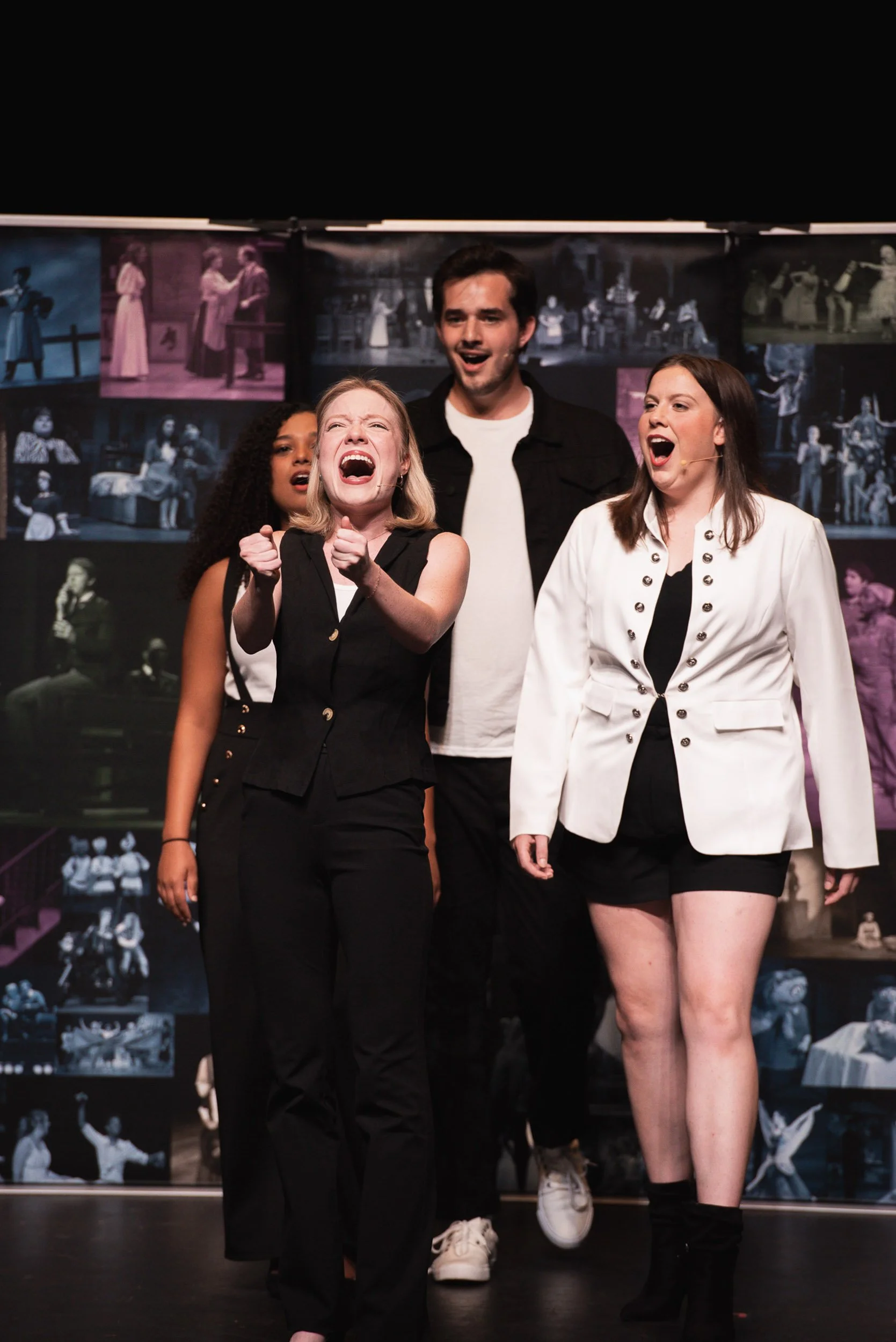 Group of four actors performing on stage with a backdrop of black-and-white photos from a theatrical production.
