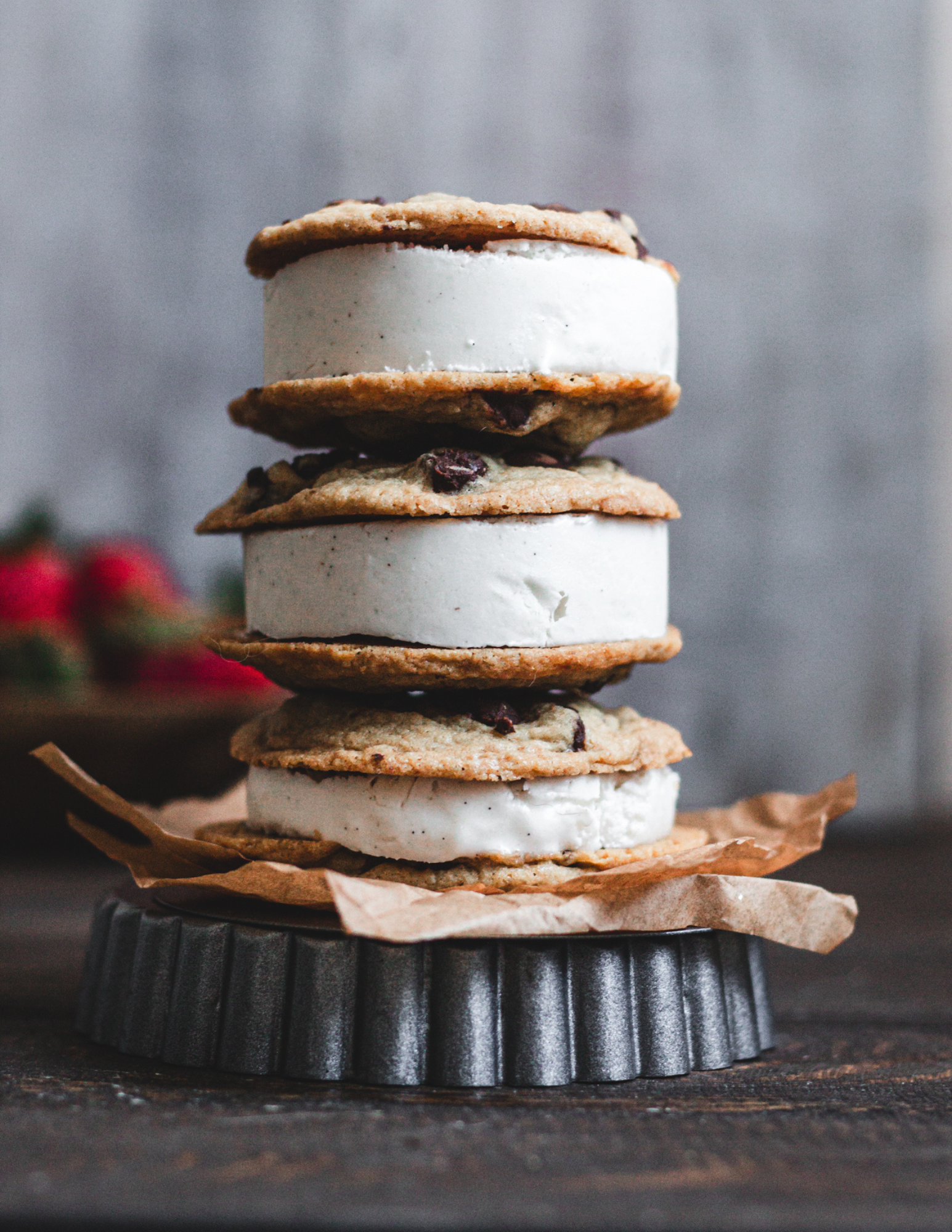 Stack of ice cream sandwiches with chocolate chip cookies and vanilla ice cream on a dark surface.