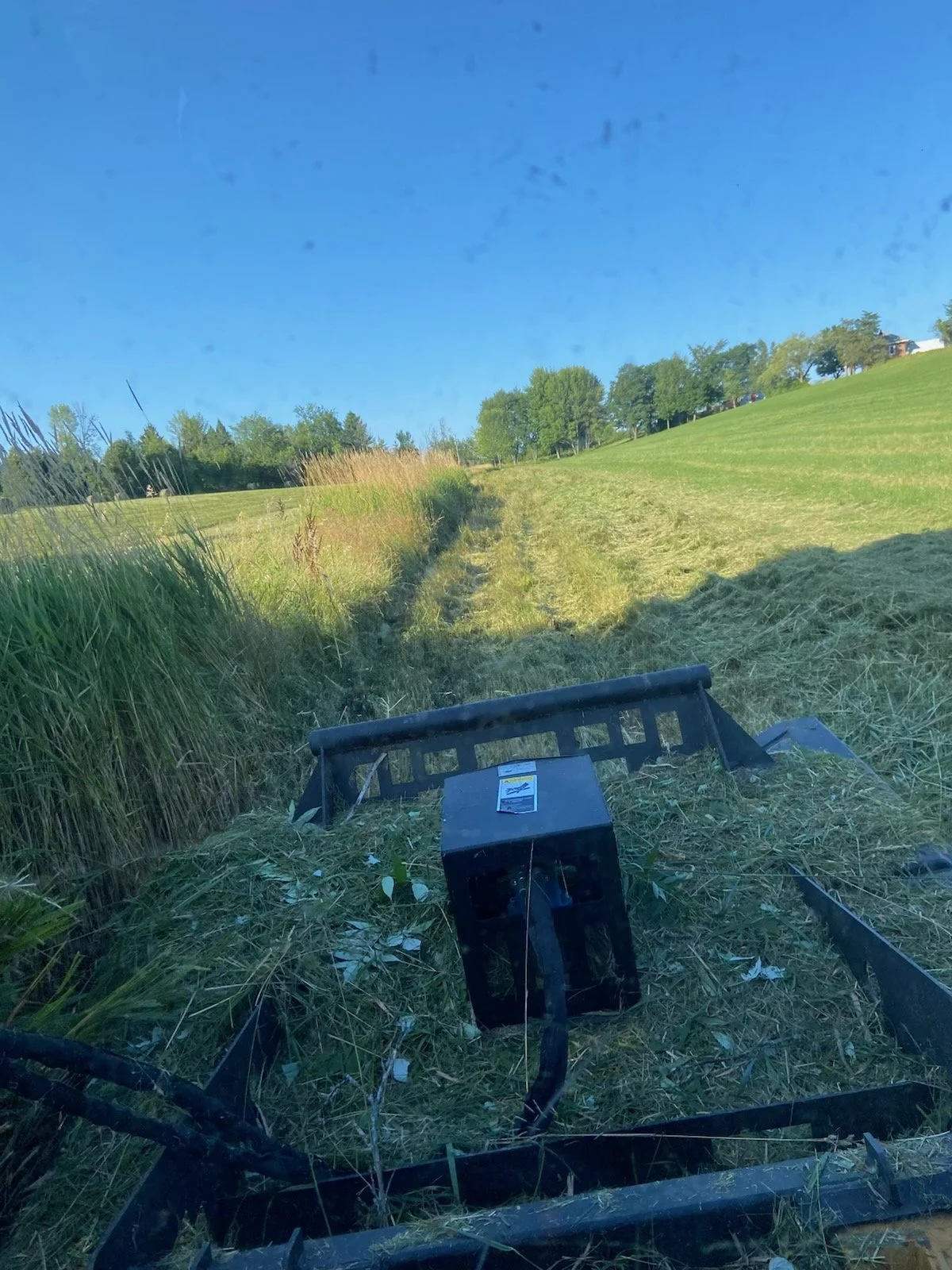 View of a field with cut grass and a blue sky, with farming equipment in the foreground.