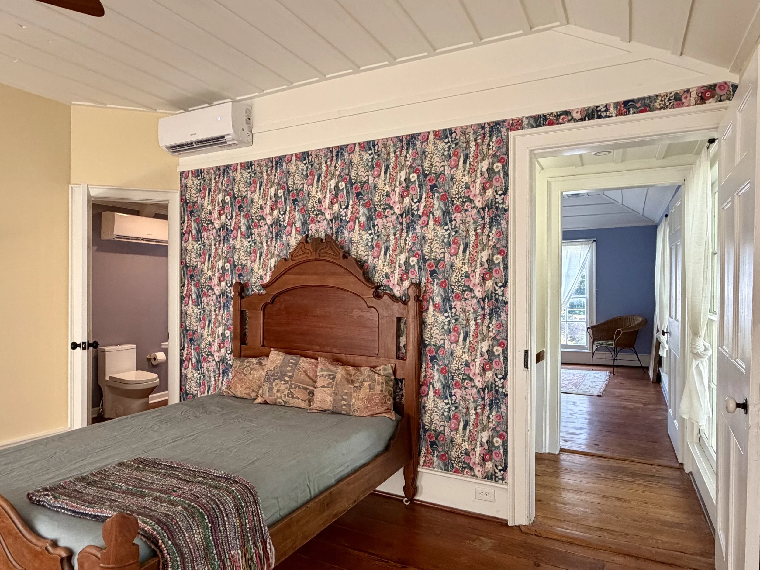 Upstairs bedroom with yellow walls, floral wallpaper, a carved wooden bed, and a doorway to the shared bathroom.