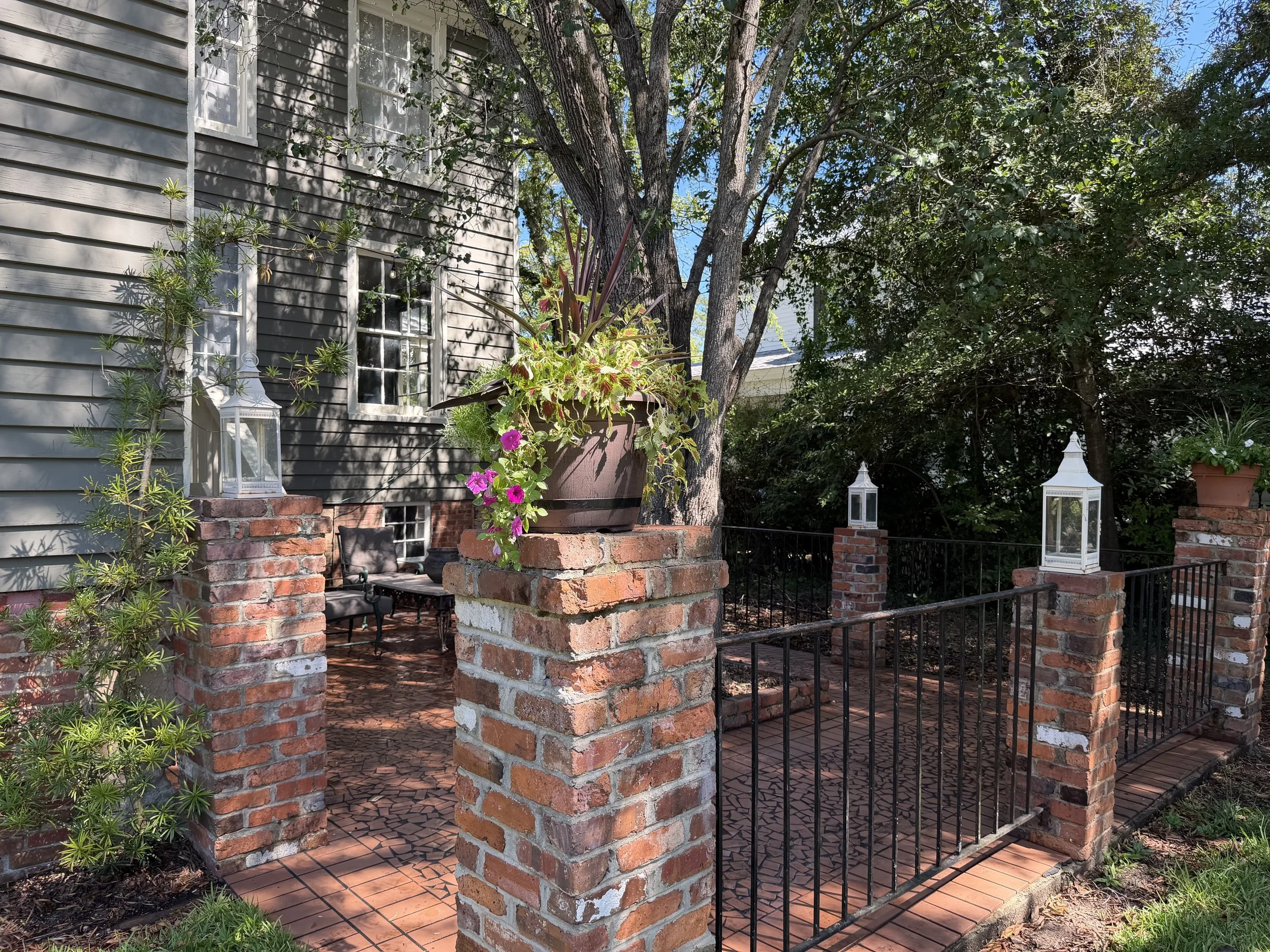 Entrance to the courtyard framed by brick pillars, white lanterns, a flowering planter, and black iron railings.