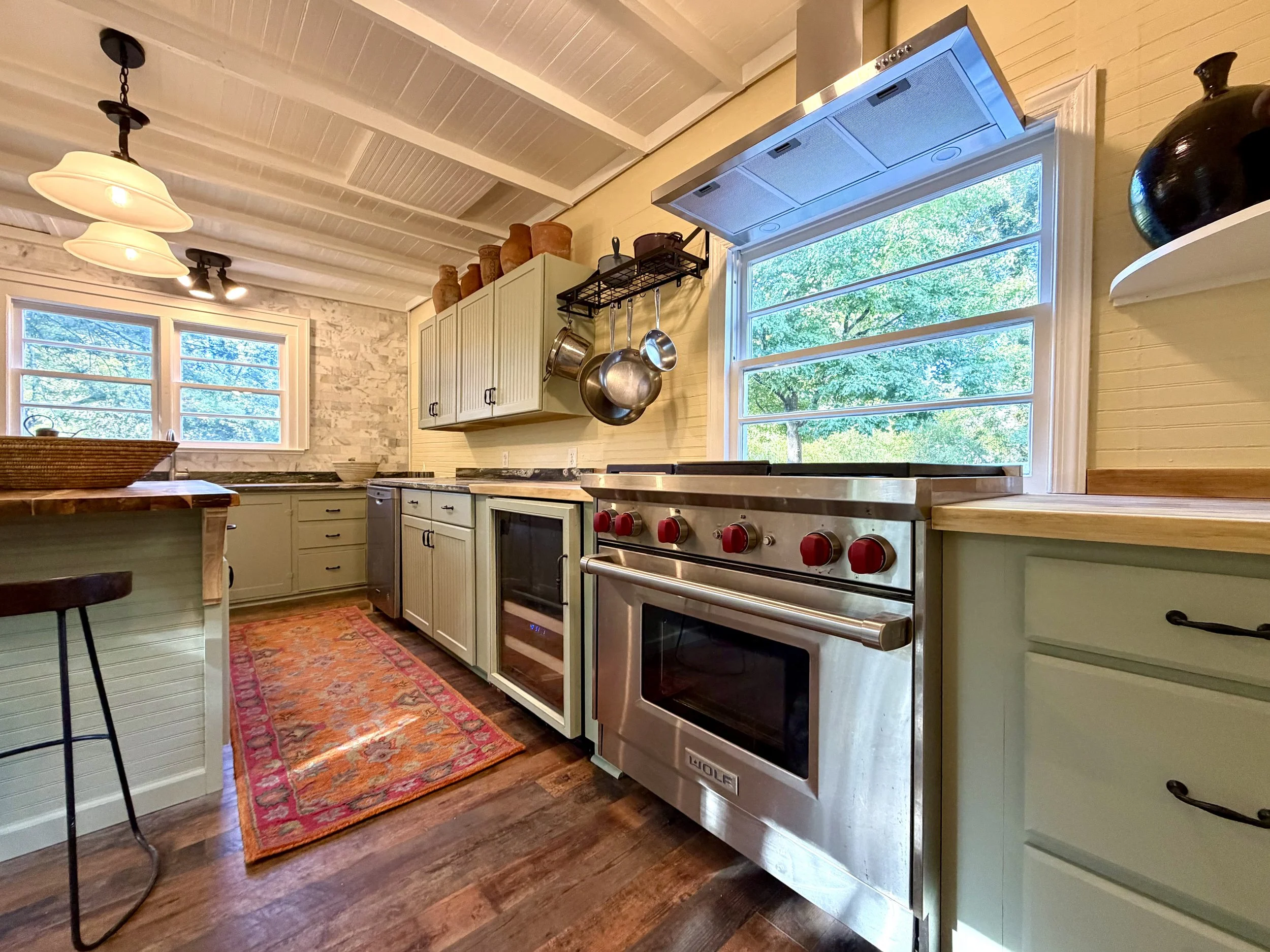 Kitchen with a stainless steel Wolf gas range, beverage cooler, pale green cabinetry, and granite countertops.