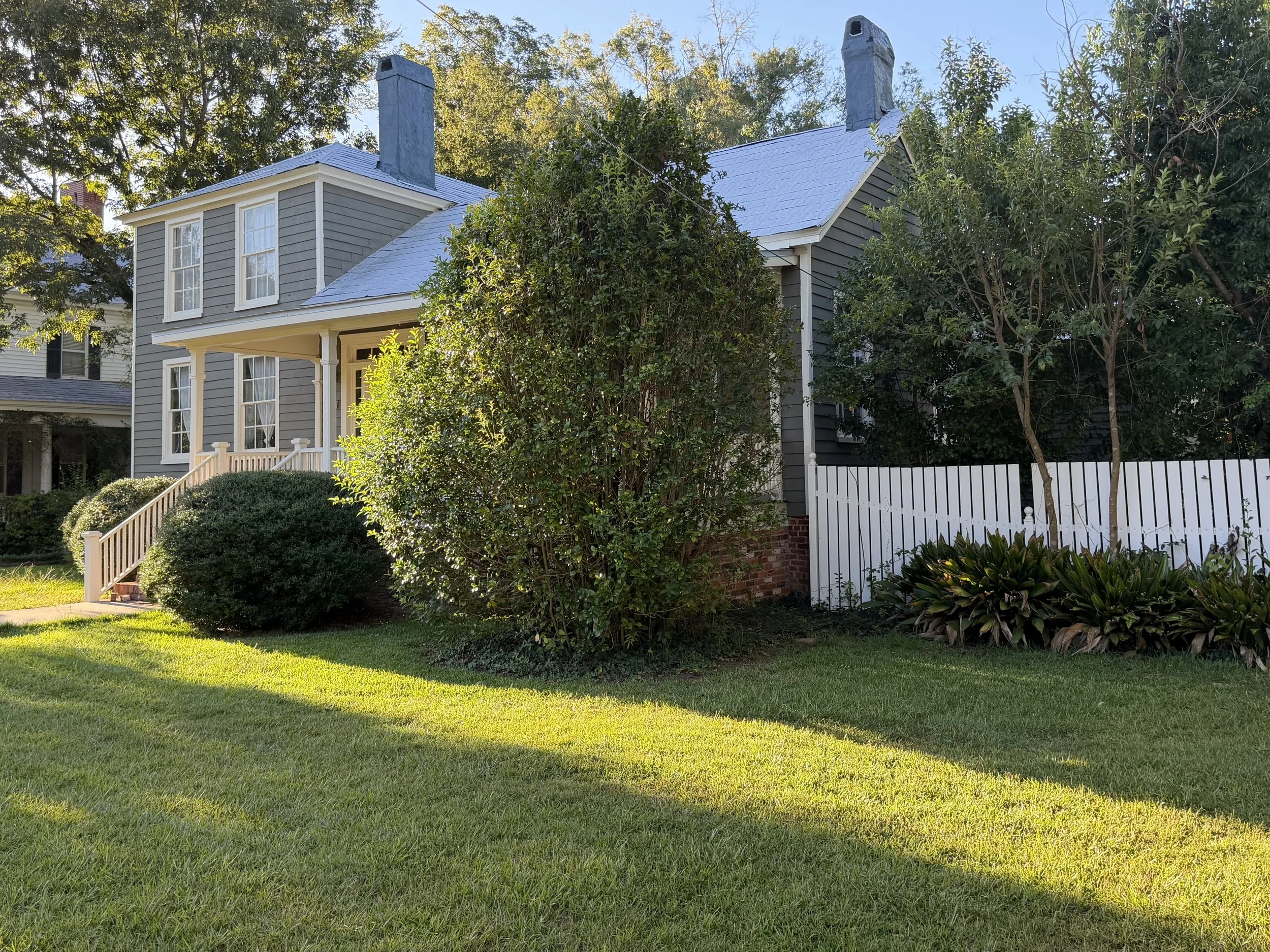 Front porch and tall windows of 212 Water Street framed by mature trees and shrubs.