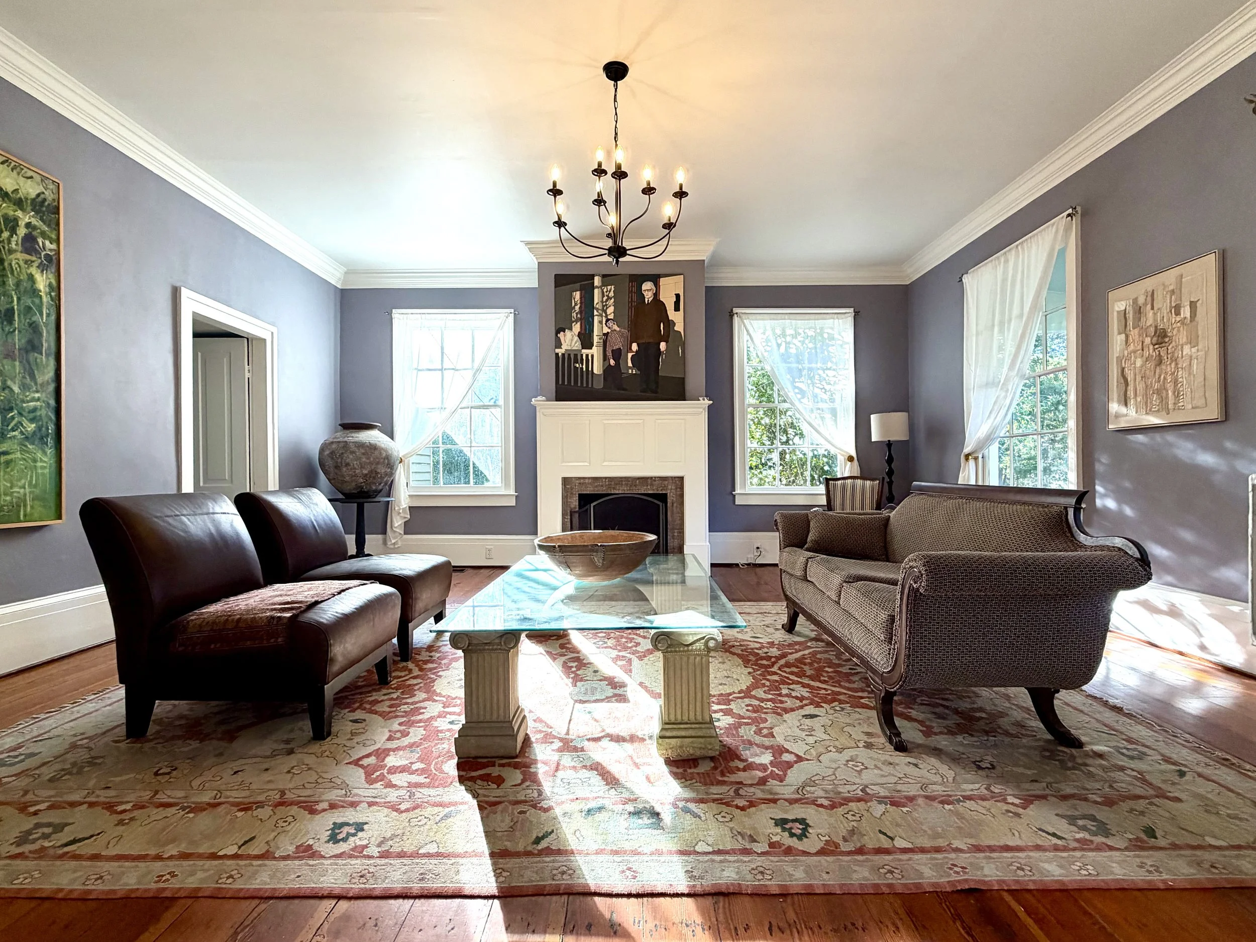 Living room with a white fireplace mantel, tall windows, heart pine floors, and seating around a glass coffee table.