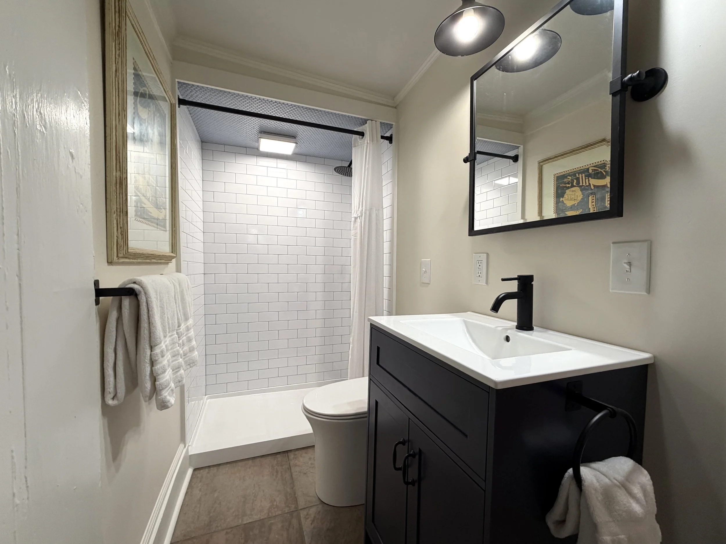 Primary bathroom with a dark vanity, black fixtures, and a walk-in shower lined with white subway tile.
