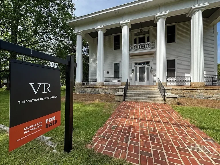 White historic house with columns, brick walkway, and a 'For Sale' sign for Virtual Realty Group in the front yard.
