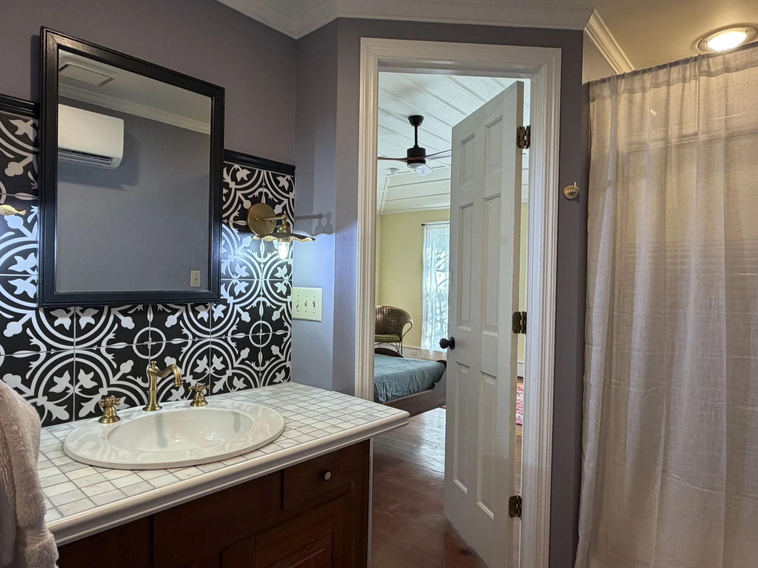 Upstairs bathroom with black-and-white patterned tile, brass fixtures, and a doorway into the yellow bedroom.