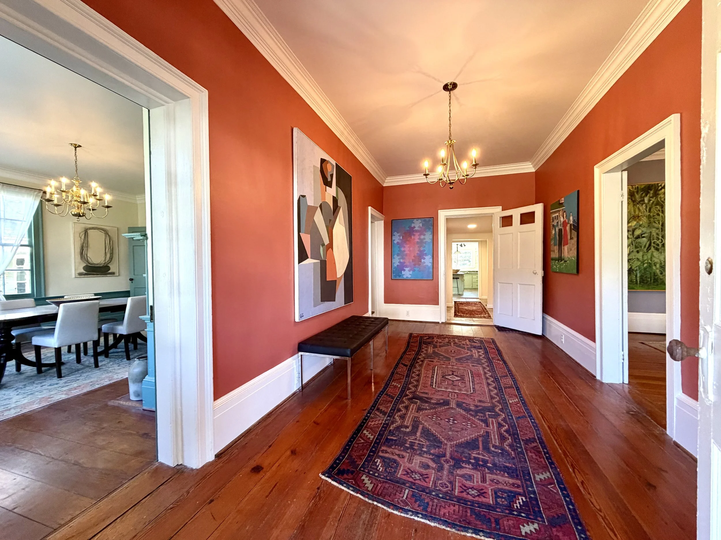 Spacious coral-painted foyer with original heart pine floors and a view into the dining room with teal trim.