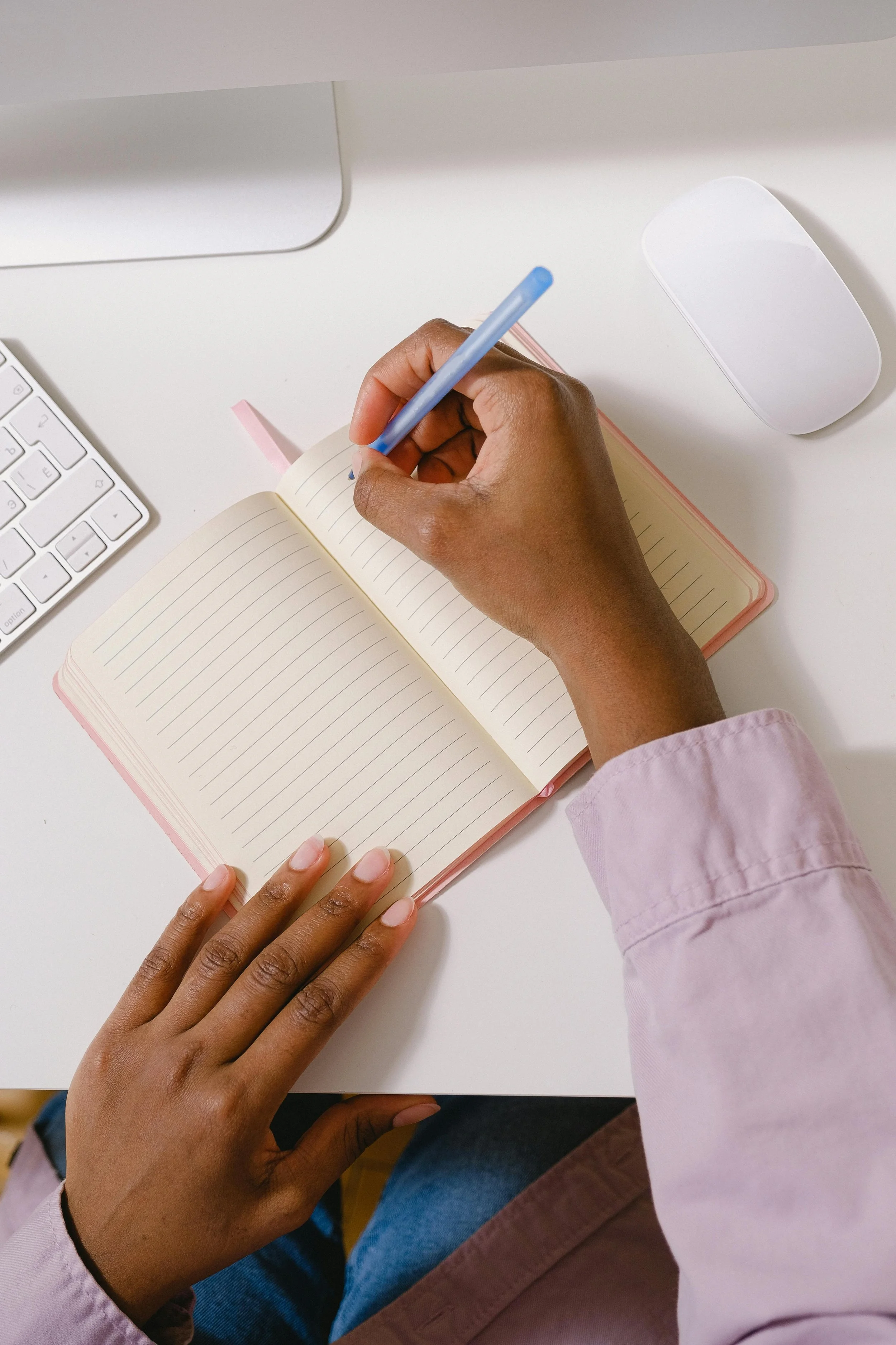 A woman with a purple shirt writing in a notebook with a pen