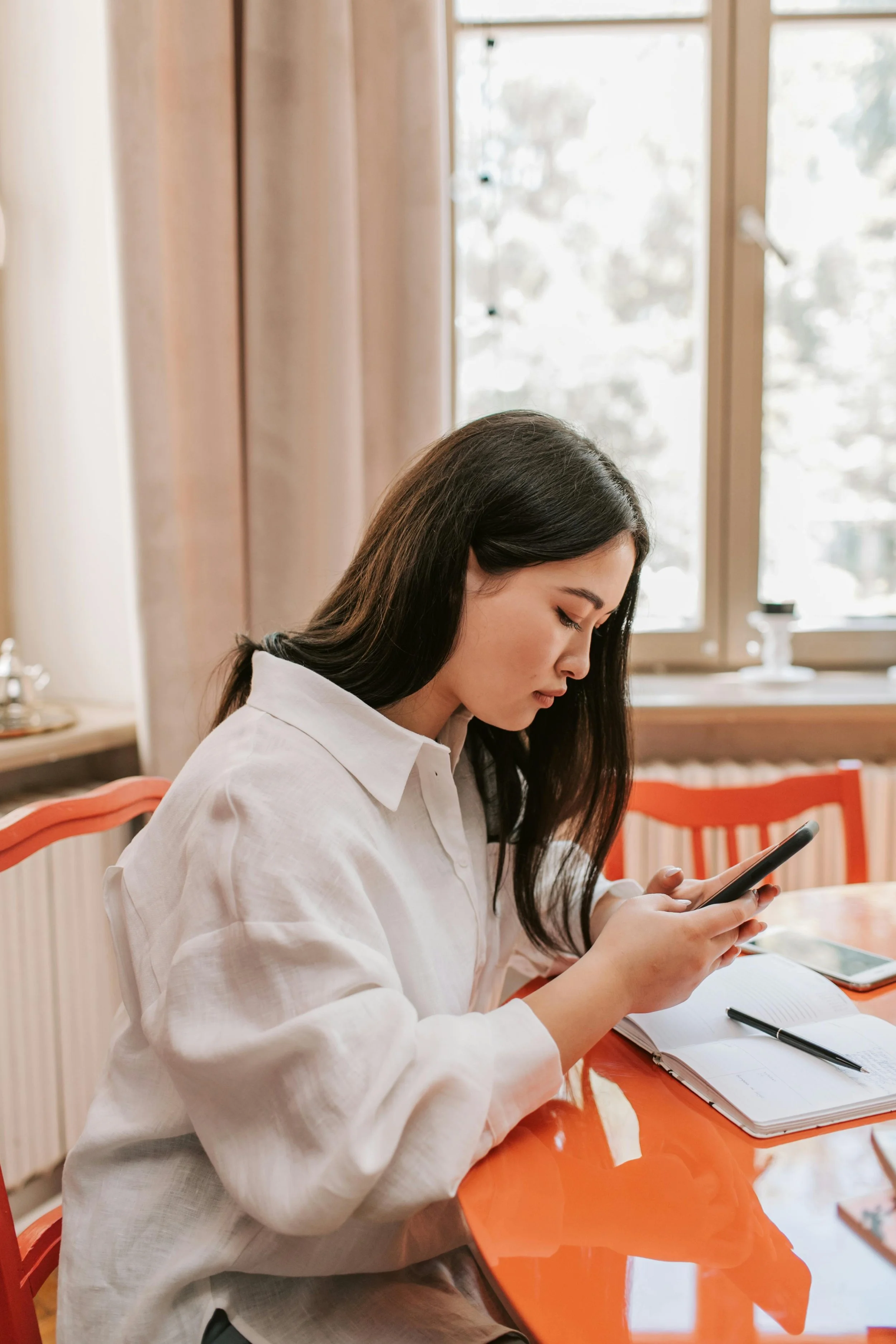 A woman with long dark brown hair and a white shirt with phone in hand