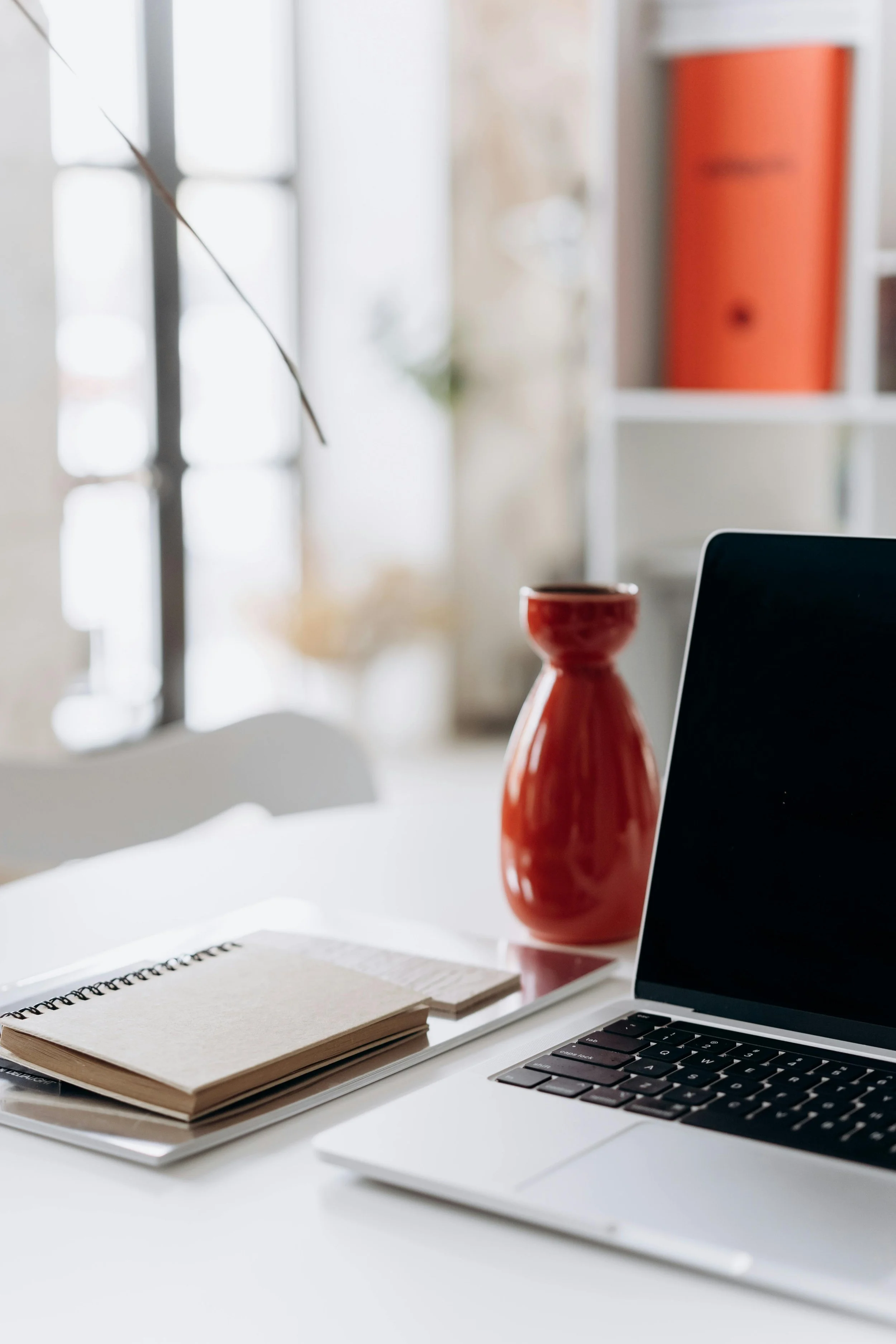 Desk with laptop, red vase, and notebook