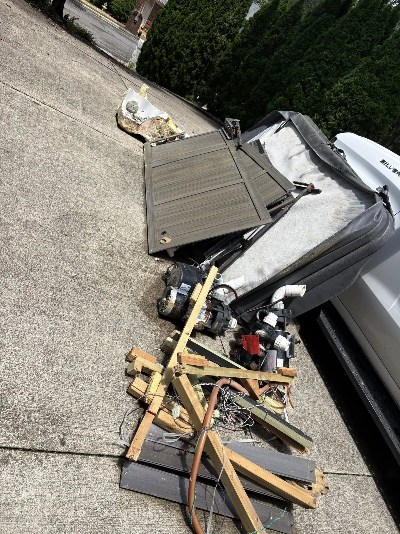 Debris from a construction or repair project on a rooftop, including wooden planks, wires, insulation, and a motor, with a partially damaged window and an air conditioning unit visible.