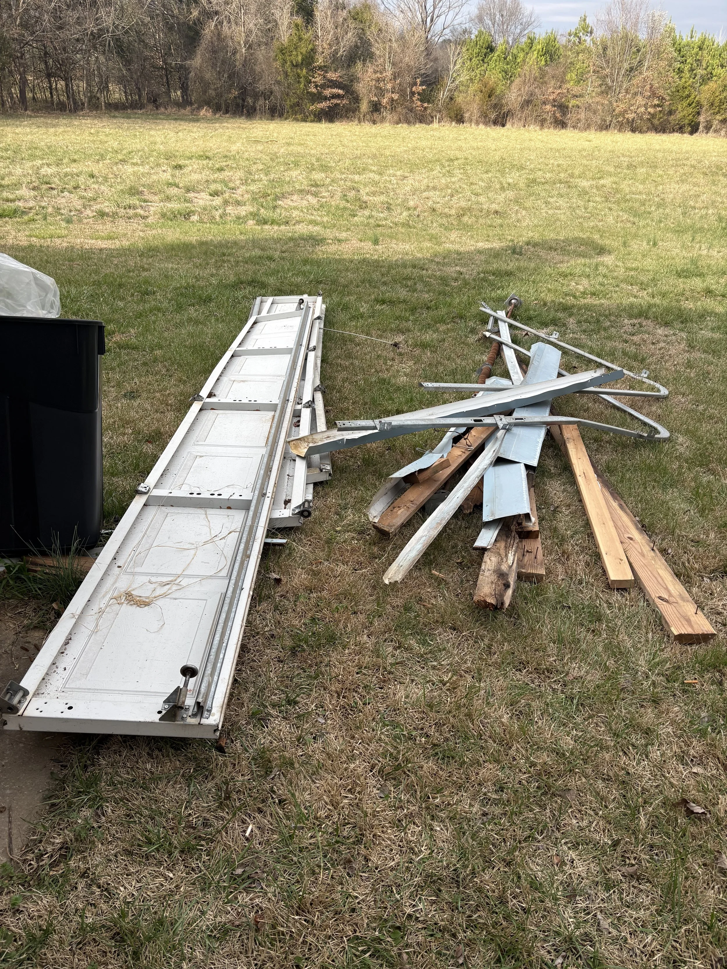Disassembled Metal ladder, wooden planks, and metal pieces scattered on grass in an open outdoor field with trees in the background.