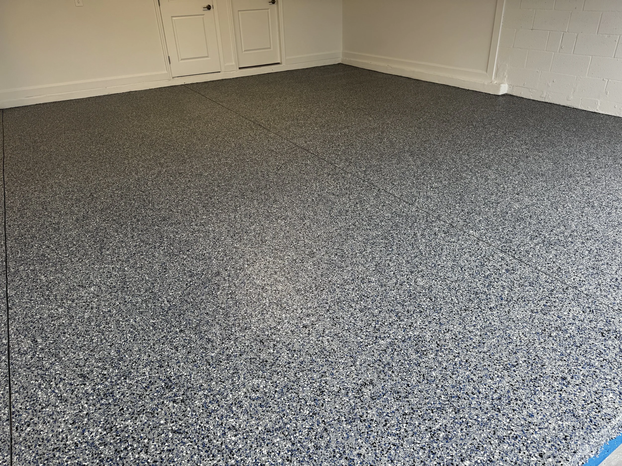 Garage with a gray speckled epoxy floor, white walls, and white cabinets or boxes along one wall. polyurea, polyaspartic