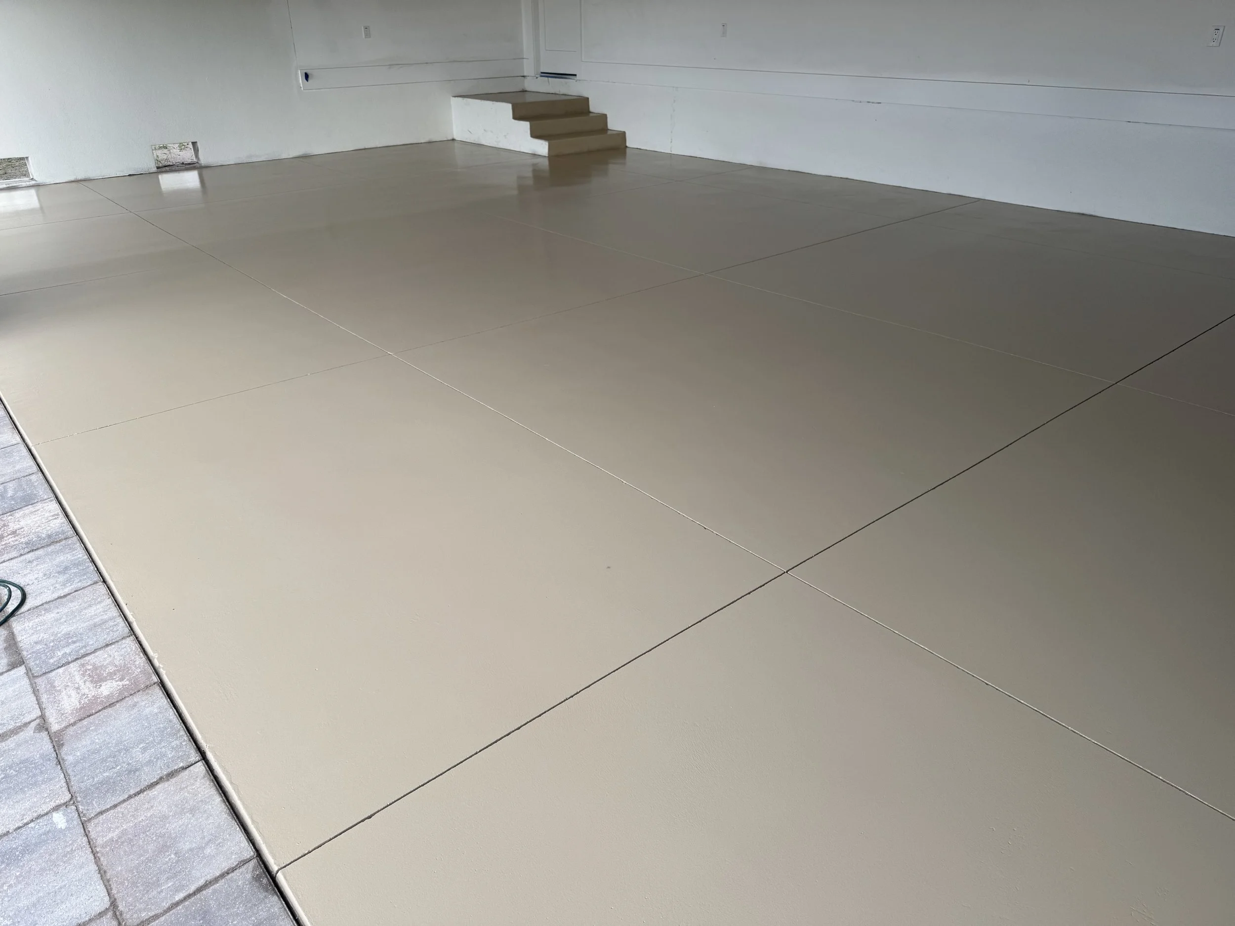 concrete slab with beige epoxy on a residential garage floor with steps in the background, and part of a brick walkway on the left.