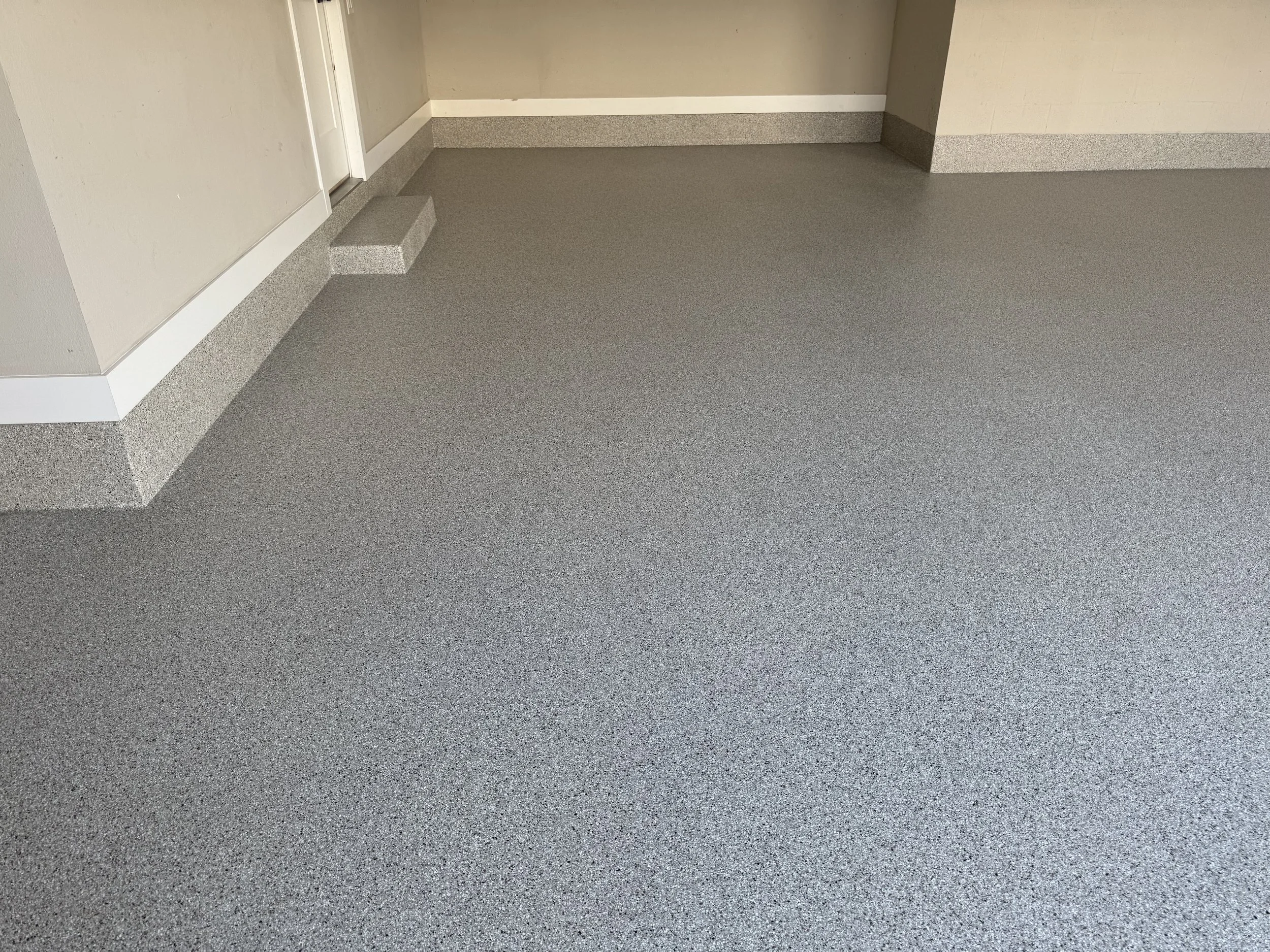 garage floor with gray speckled epoxy flooring, beige walls, and a raised step near the corner. epoxy, polyapartic, polyurea, epoxy floors near me, tampa bay area