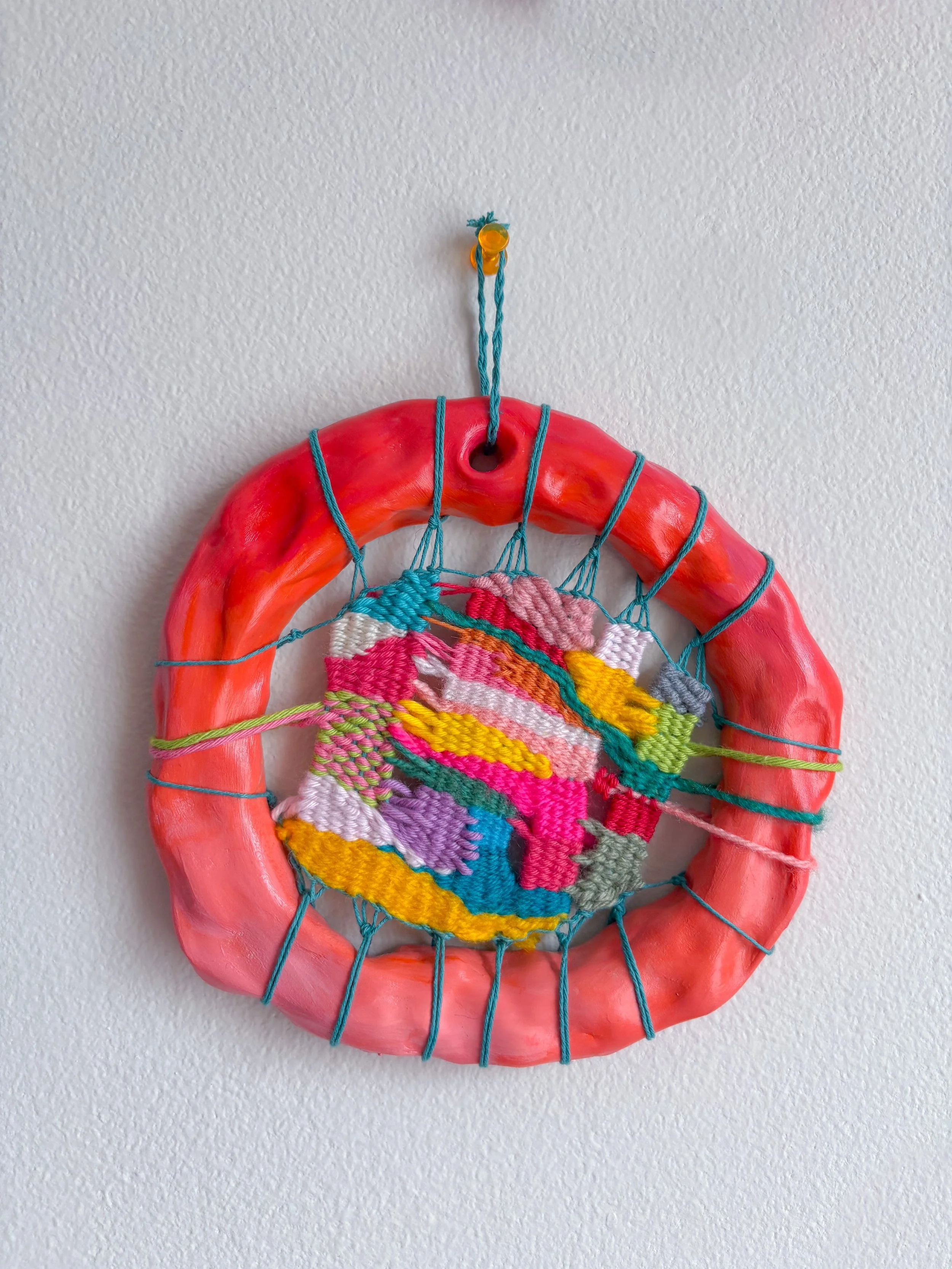 "Old friendships, new beginnings, and sparkling water in colorful champagne glasses. Seeing progress after working on something for a long time. A really good hug." --- Emerging (2025). 6" x 6" x 1".	Thread, yarn, clay, acrylic paint, and glue.