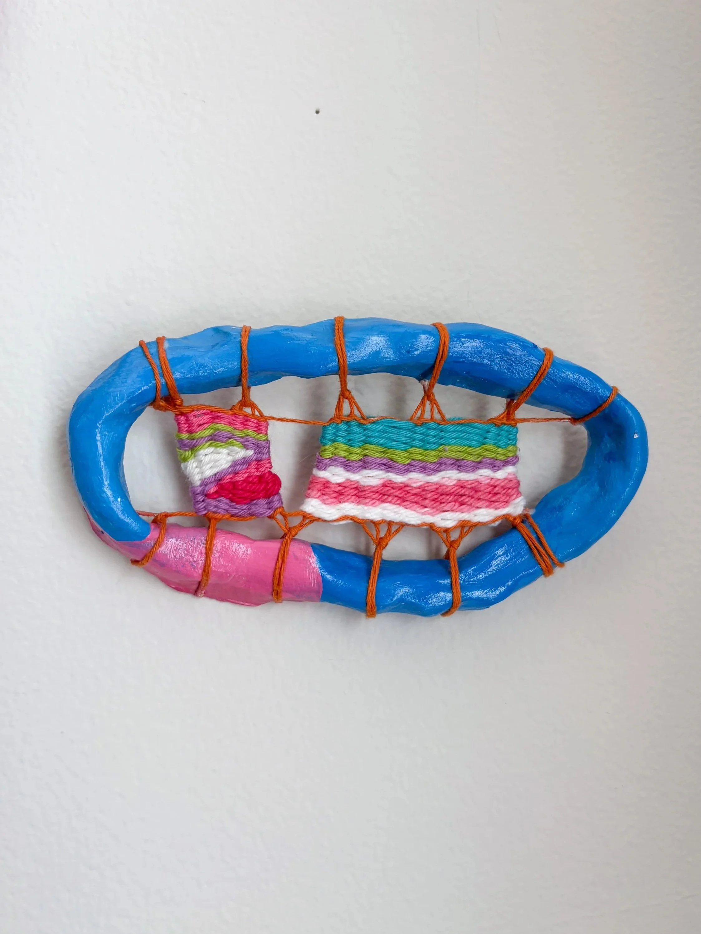 "Holding hands on a bench by the lake, on a sunny day, under the shade of a leafy tree." ---- Pink Stripe (2025). 5.75" x 3" x .75". Thread, yarn, clay, acrylic paint, and glue.  Available in shop.