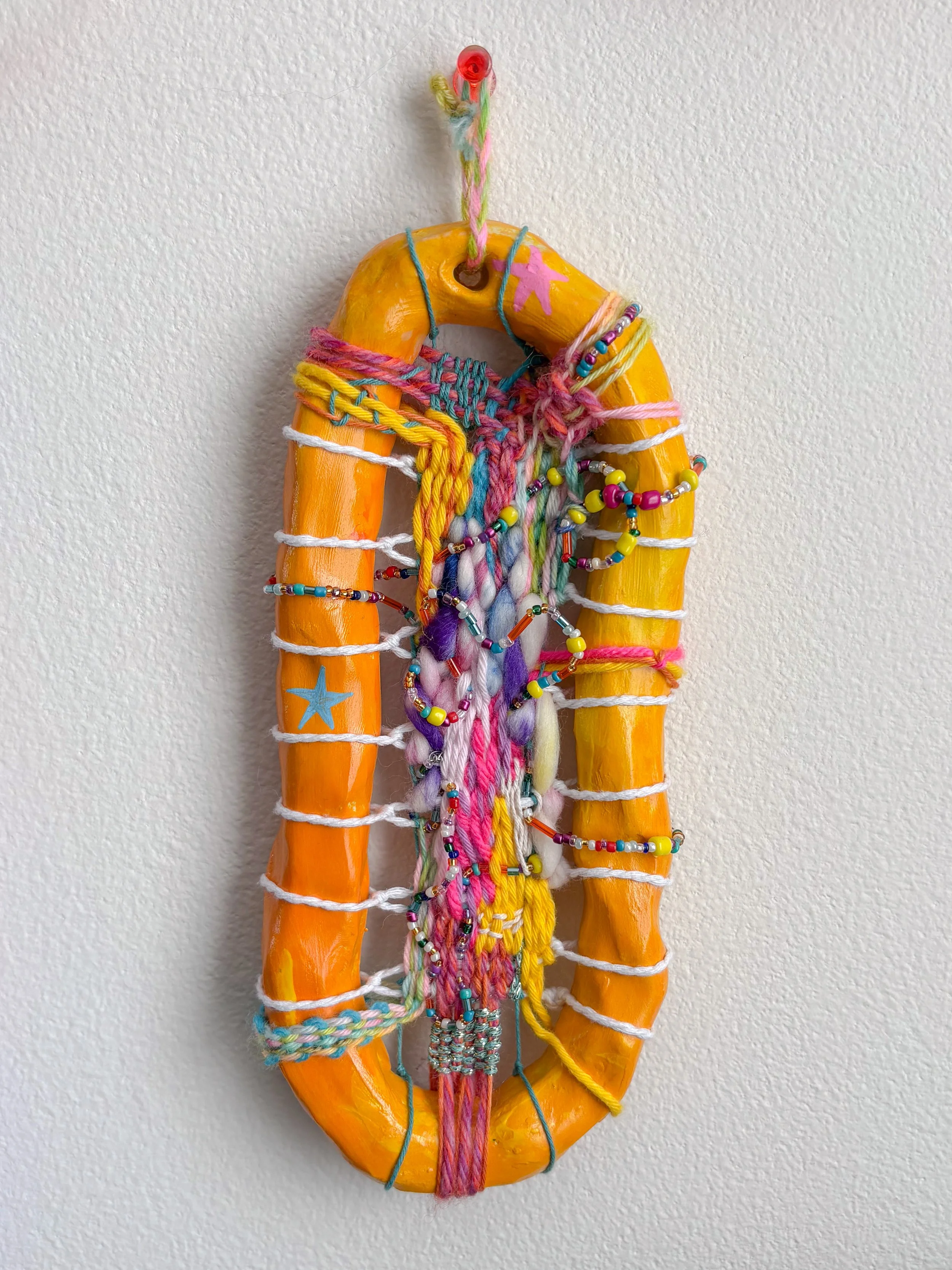 "Finding something to smile about. Playing around. Exploring and communing and sharing." --- Play (2026). 8.25" x 3.75" x 1". Thread, yarn, clay, acrylic paint, beads, wire, and glue.