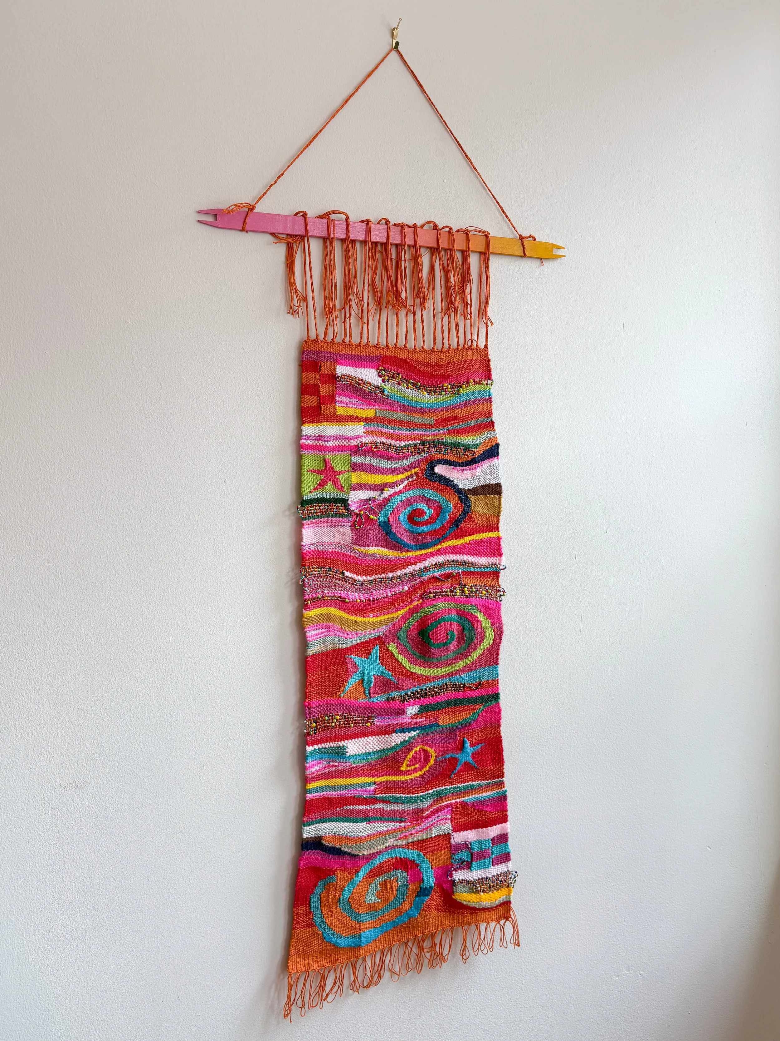 Oranges and Cinnamon, Spirals and Stars (2026). 11" x 31" x .45". Yarn, thread, beads, and wire.