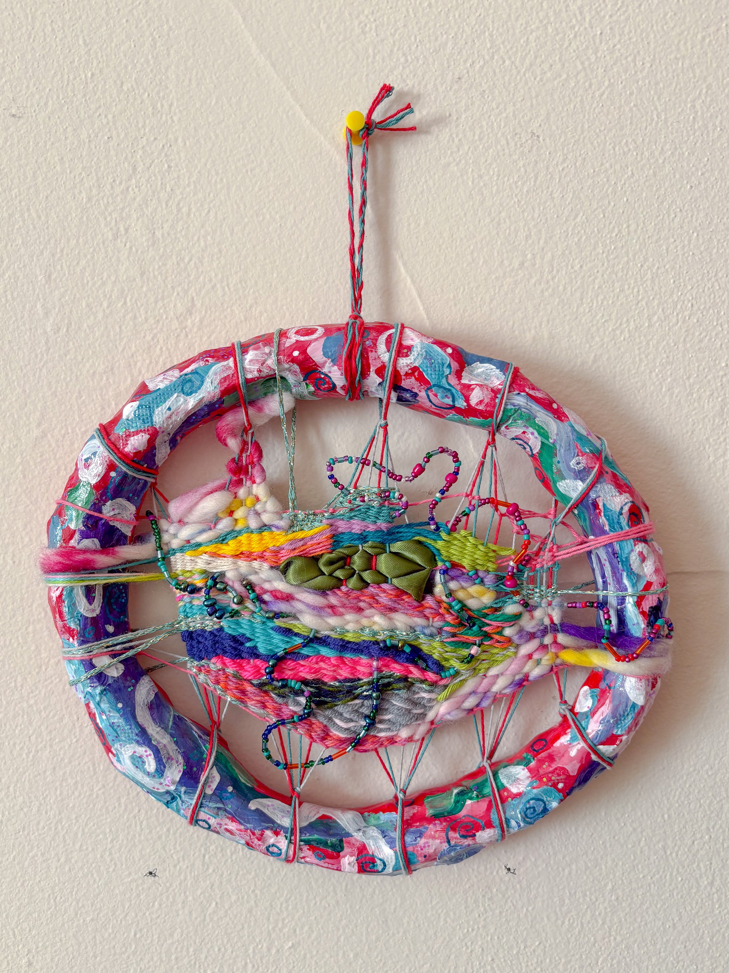 "Swirling with an excess of energy. Ready to jumpstart your day with a great attitude. Alignment with the universe and your higher self." --- Abundance	(2026). 8" x  9" x 1.25". Thread, yarn, clay, wire, beads, acrylic paint, ribbon, glitter, and glu