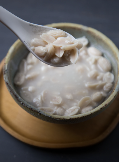 A spoonful of white bean soup with creamy broth in a ceramic bowl on a wooden tray.