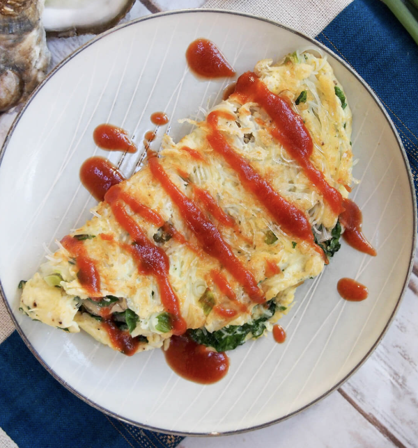 Omelette with cheese, green onions, and spinach, topped with ketchup, served on a white plate.