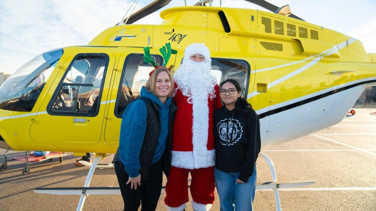 Denver Children’s Foundation volunteer with a child and Santa in front of a helicopter at a Christmas for Kids event