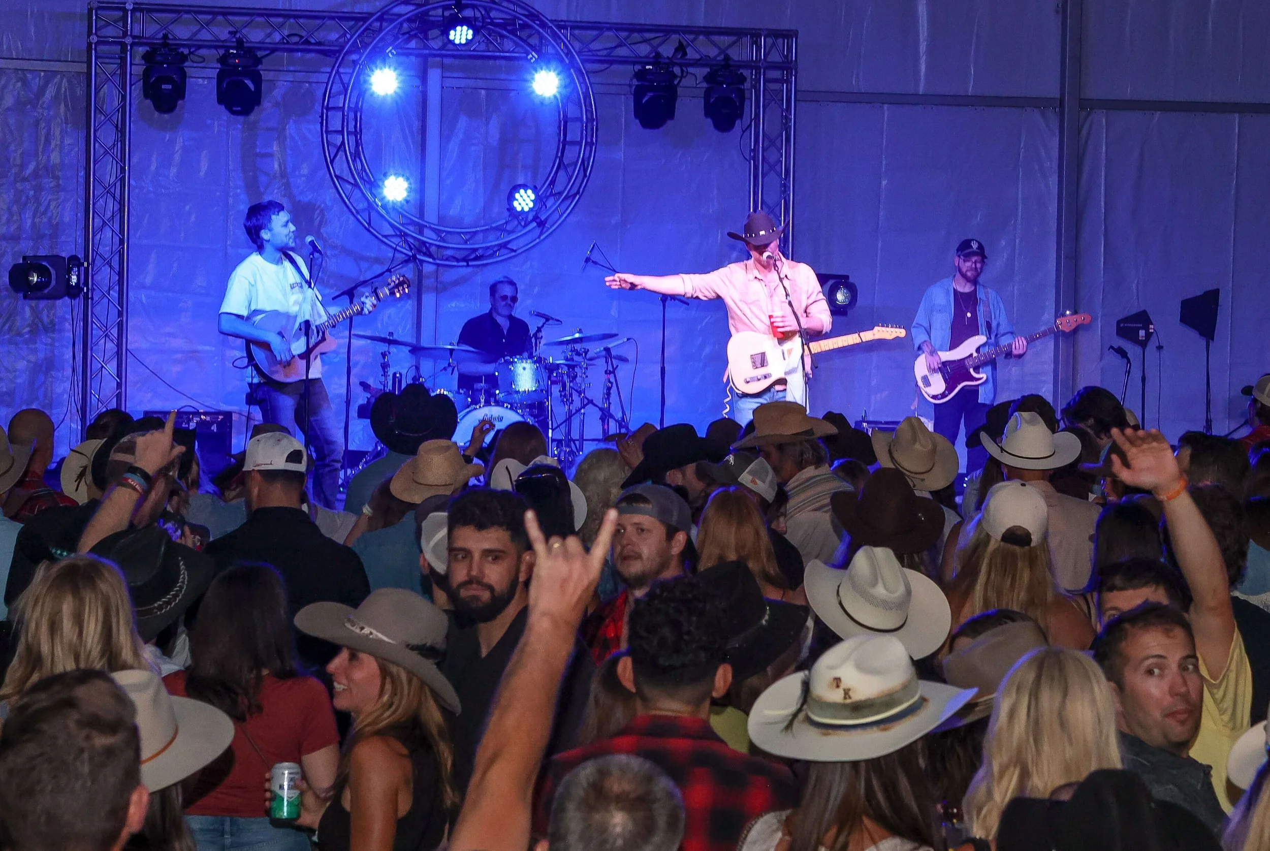A band performing on stage at a concert with a crowd of fans wearing cowboy hats in the audience.