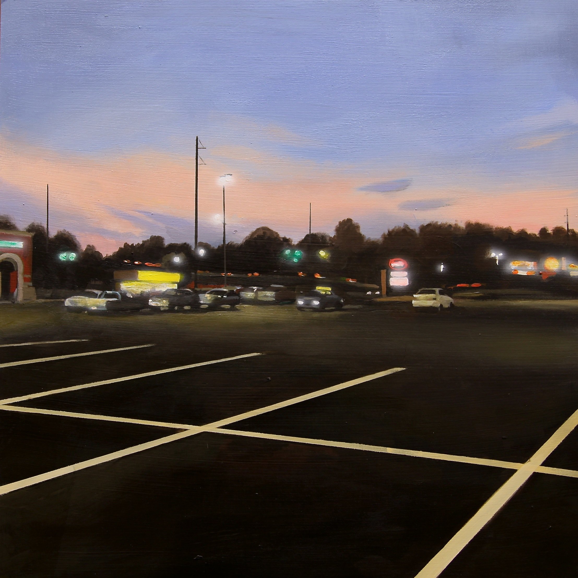 Enlarged view of a parking lot during sunset with empty spaces in the foreground, and several parked cars, illuminated businesses, and a sky with orange and blue hues in the background.