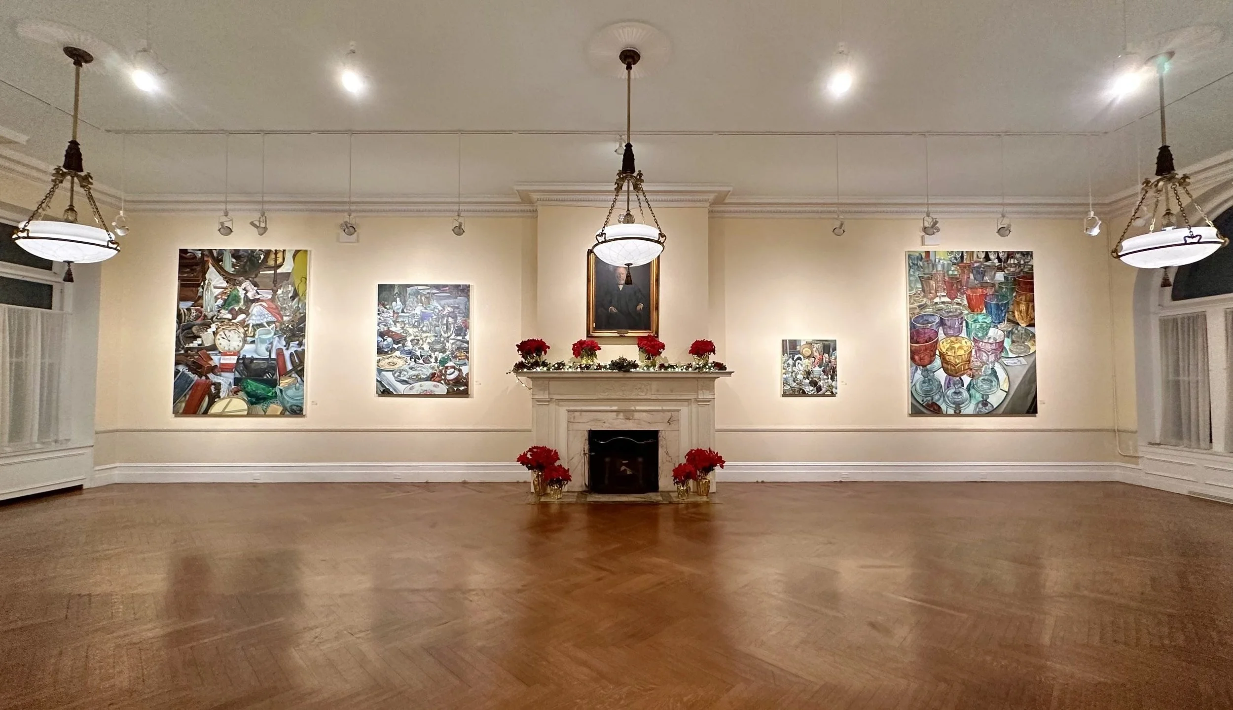 An art gallery room with a decorated fireplace mantel, poinsettias, framed artworks of glass and clutter, and overhead lighting.