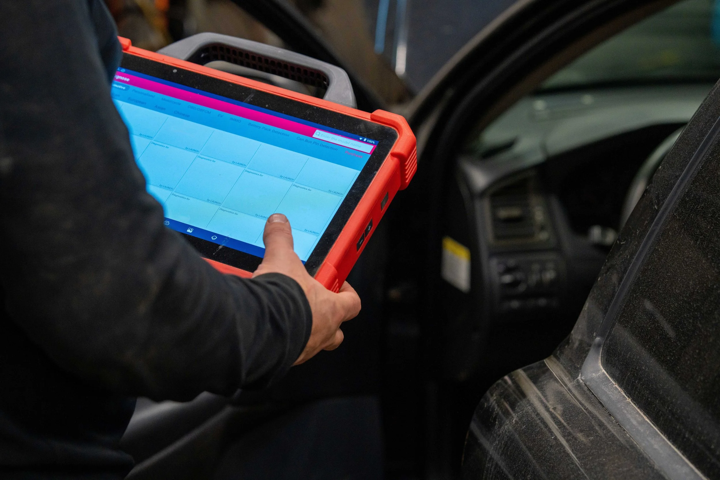 Person holding a diagnostic scanner inside a vehicle, inspecting the vehicle's systems.