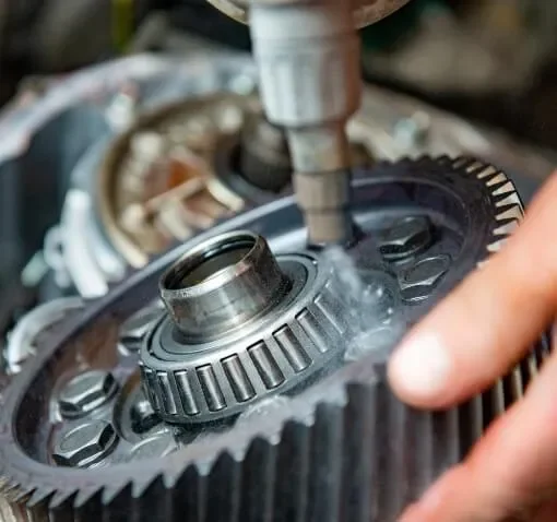 Close-up of a mechanical gear assembly being worked on, with a person's finger pointing at the gear.