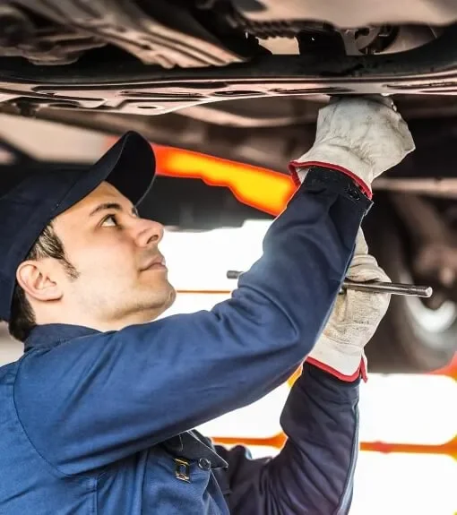 Automotive mechanic working underneath a vehicle, using a tool with a focused expression.