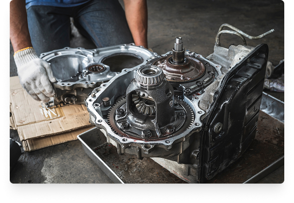 A person working on a disassembled car transmission placed on a workbench in a garage or workshop.
