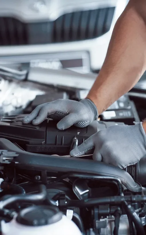 A mechanic wearing gray gloves working on a car engine.