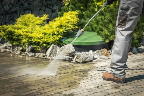 Person pressure washing a brick patio with a green spray nozzle