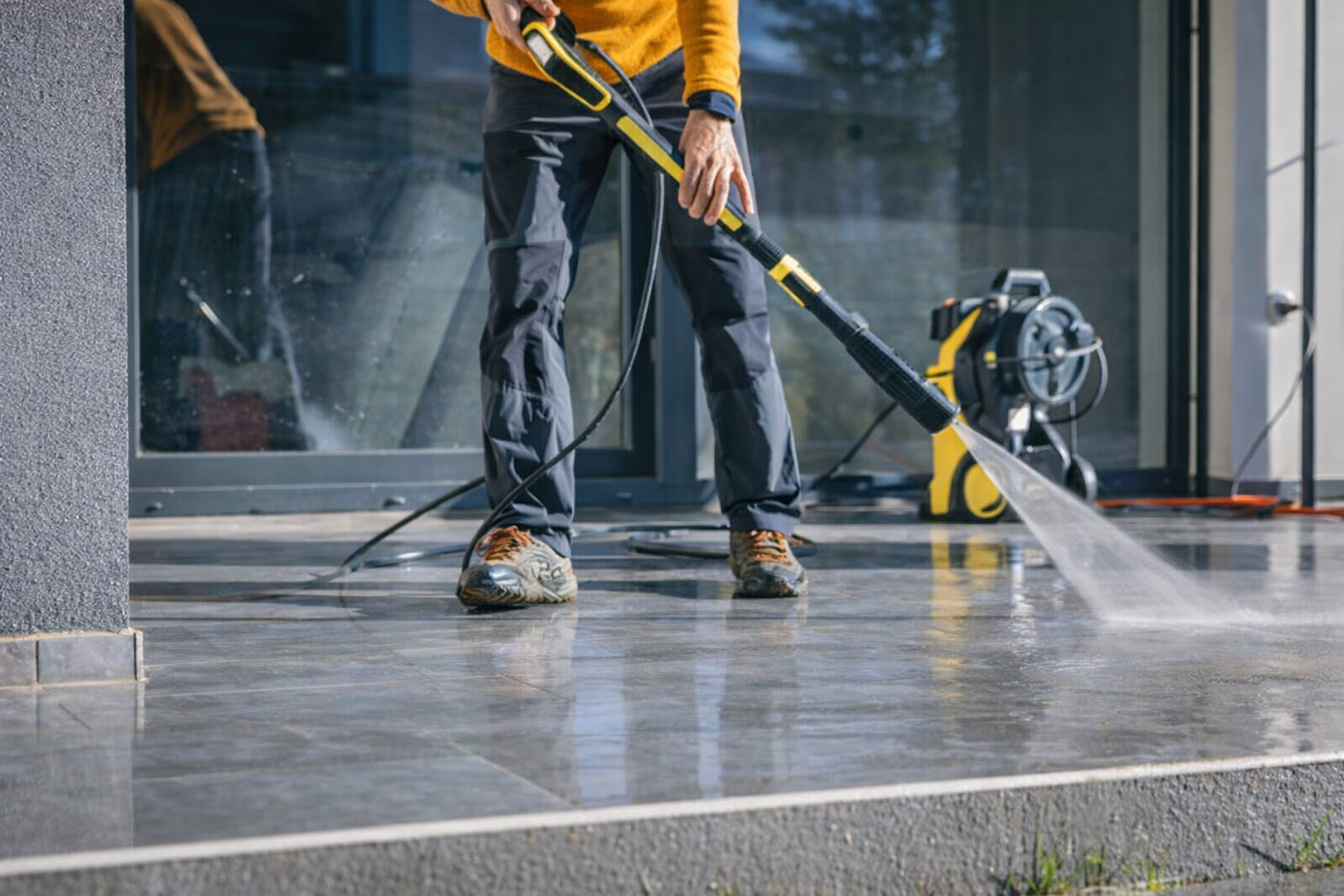 Person in yellow jacket cleaning a glass outdoor surface with a power washer.