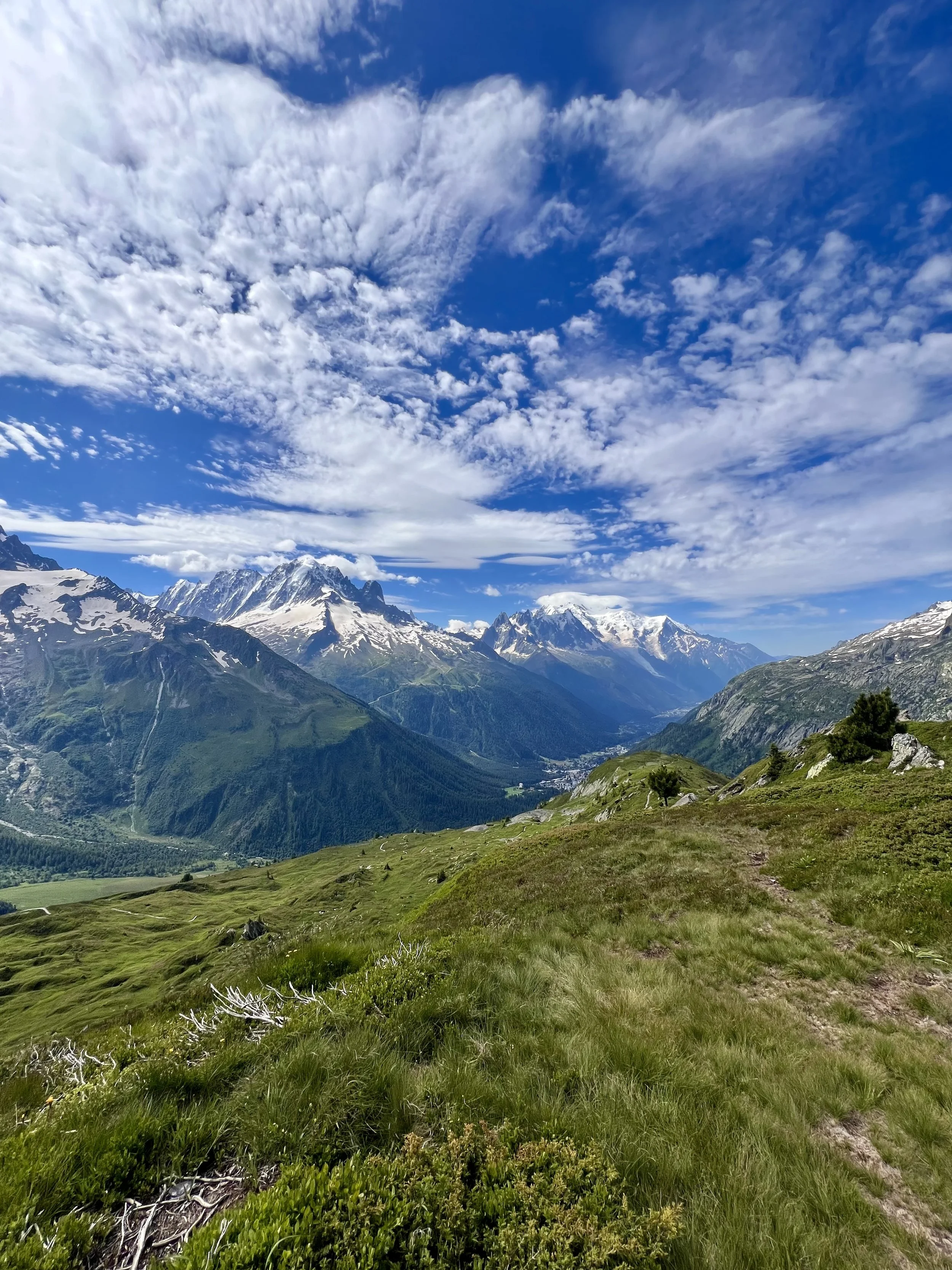 Scenic mountain landscape with snow-capped peaks, green valleys, and a blue sky with scattered clouds.