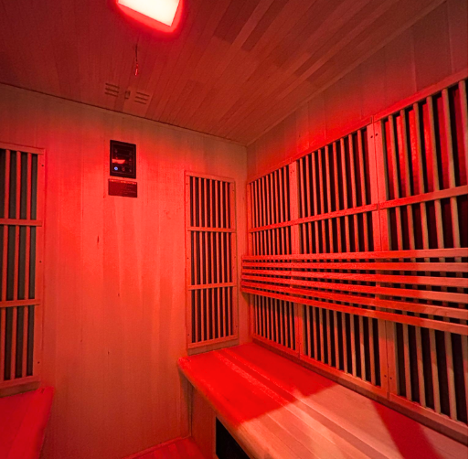 Interior of a wooden sauna room with red lighting, wooden benches, and slatted walls.