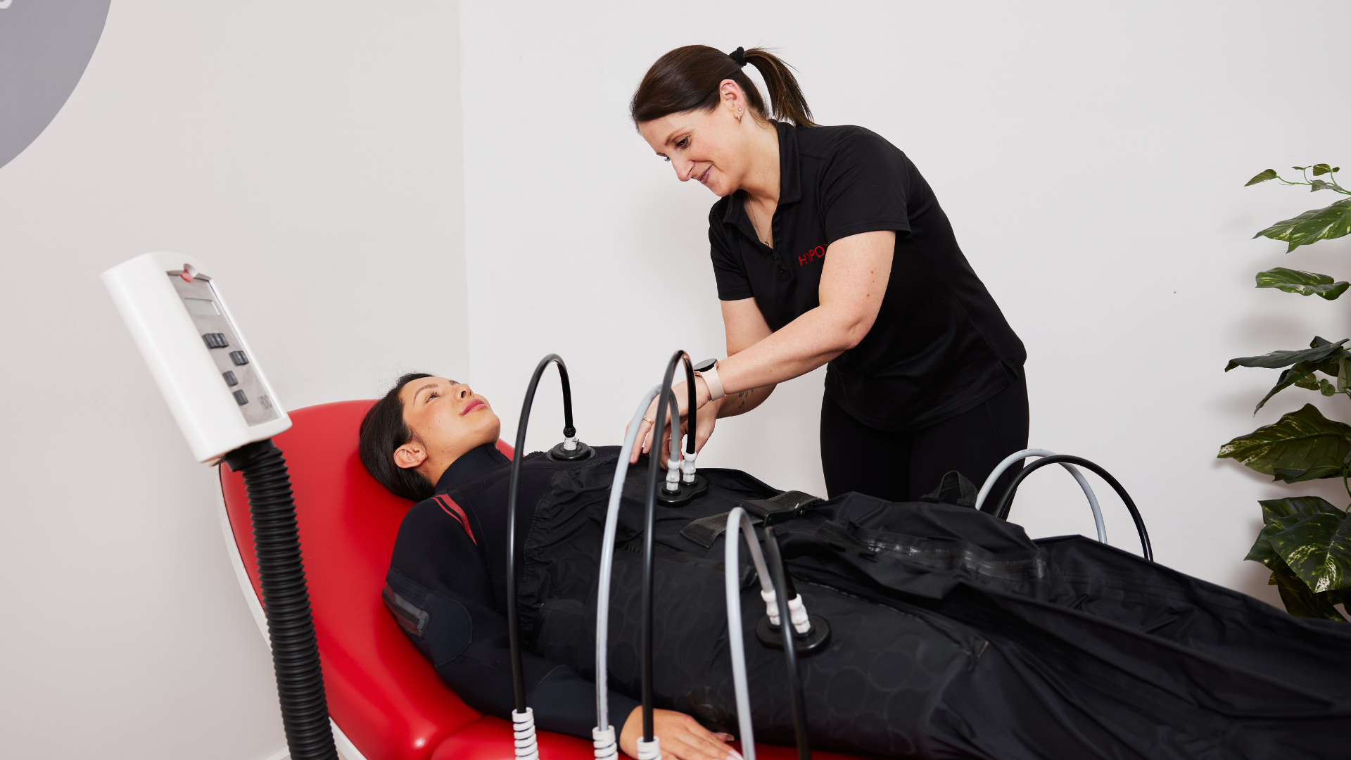 A woman lying on a medical treatment bed with her arm being connected to a machine by a technician.