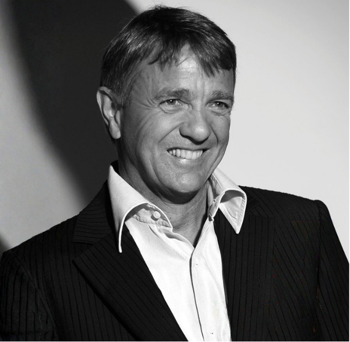 Black and white photo of a man in a suit smiling, with short hair and a collared shirt.