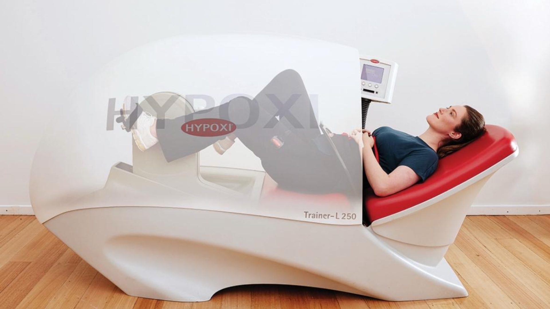 A woman lying on a hyperbaric oxygen therapy chamber with her eyes closed, connected to a monitor for treatment.