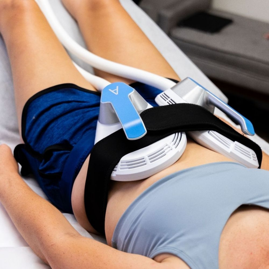 A person lying on a medical bed with a ventilator or breathing machine device secured around their abdomen.