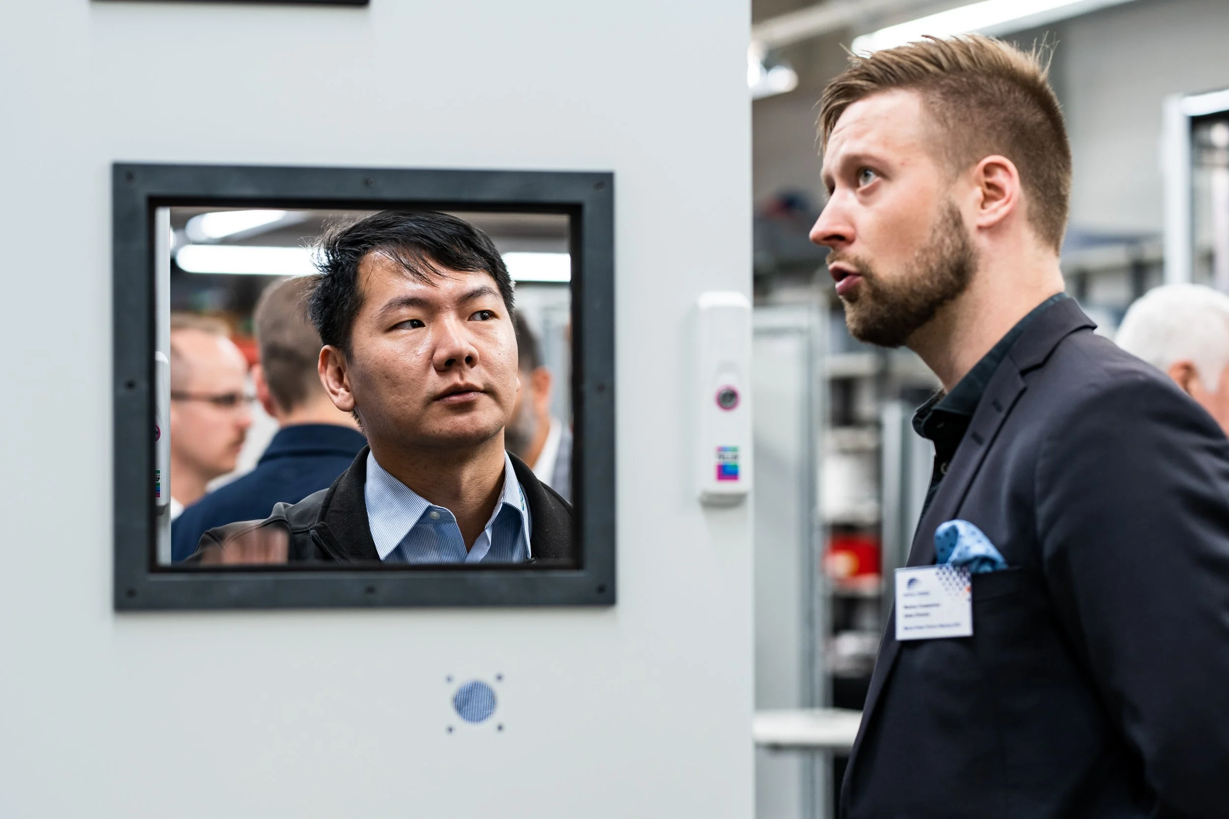 Two men in conversation at a business event, one looking through a security scanner, the other standing nearby.
