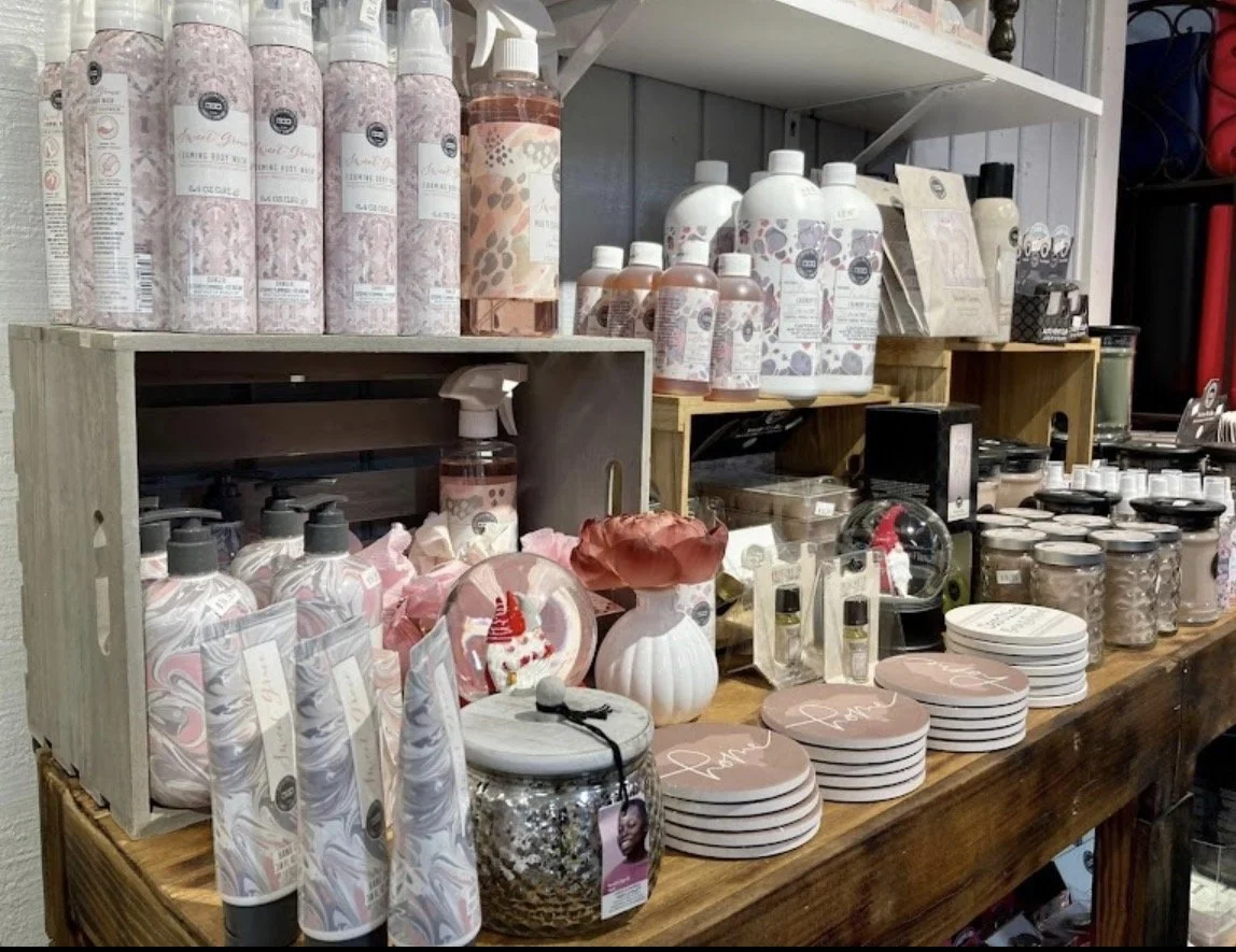 A display of various personal care products, candles, plates, and decorative items on a wooden table and shelves in a retail store.