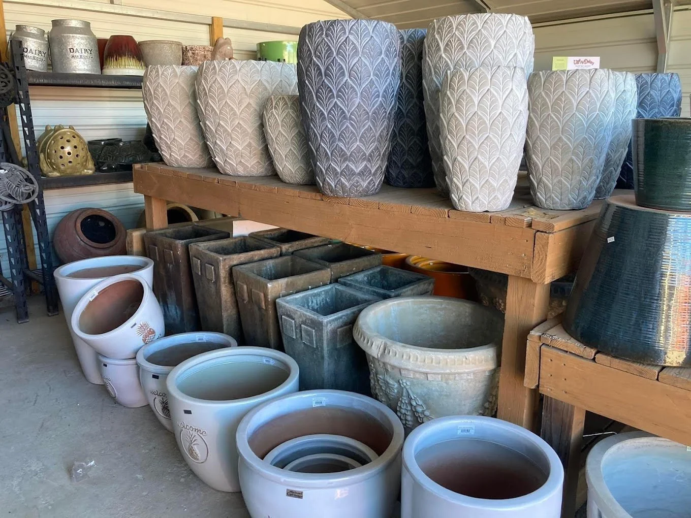 Large decorative planters and flower pots displayed on wooden shelves and on the floor, including some with floral and geometric patterns