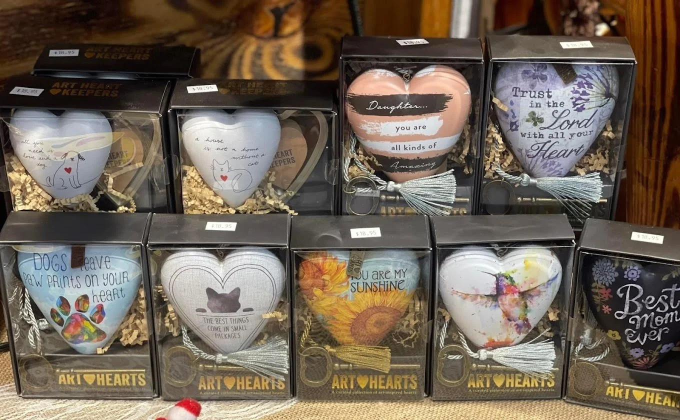 A display of nine decorative heart-shaped ornaments in boxes with quotes and designs, featuring animals, flowers, and inspirational messages, each with a small tassel and keychain attachment.