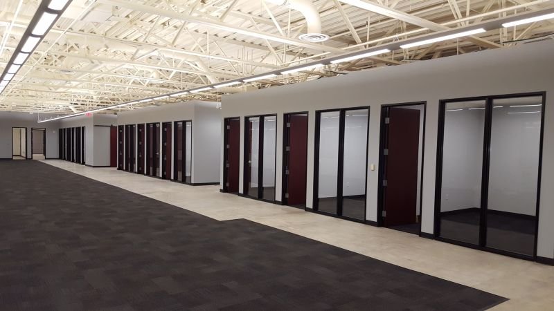 Empty office corridor with glass-walled individual offices and exposed ceiling beams.
